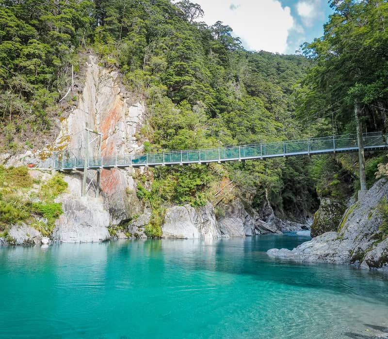 Suspension bridge over clear turquoise river with dense green forest and rocky cliffs