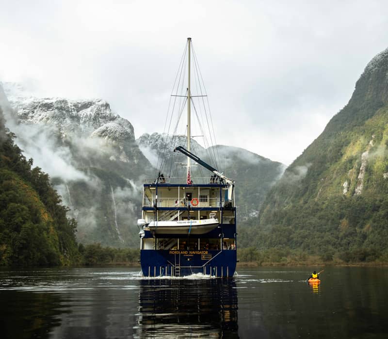 Cruise ship in New Zealand's South Island amidst misty mountains.