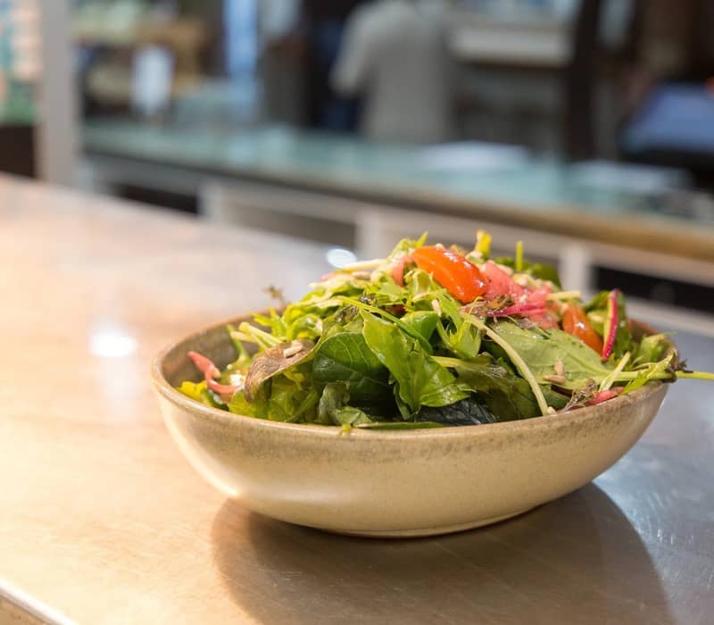 Bowl of fresh mixed green salad with tomatoes and seeds on countertop