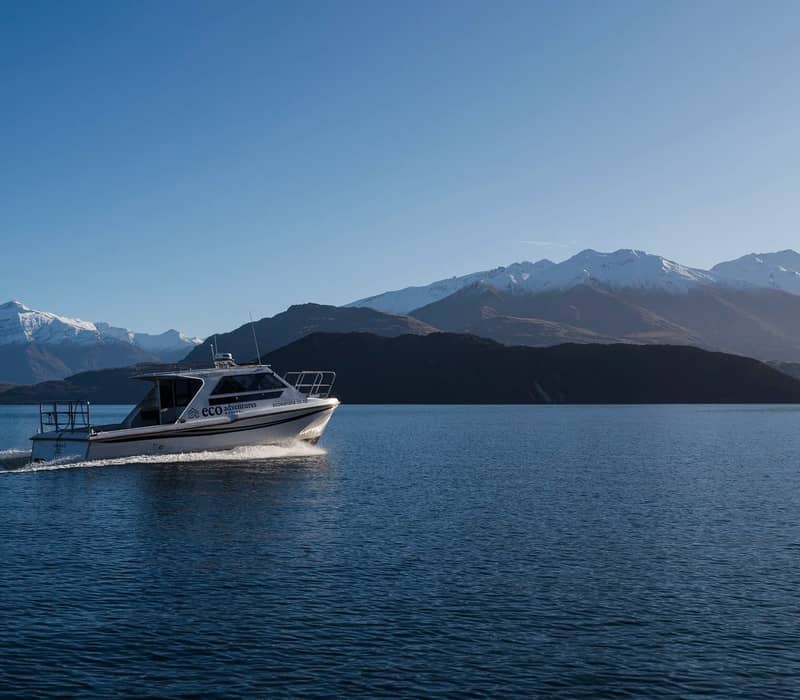 Motor boat on lake with snow-covered mountains under clear blue sky.