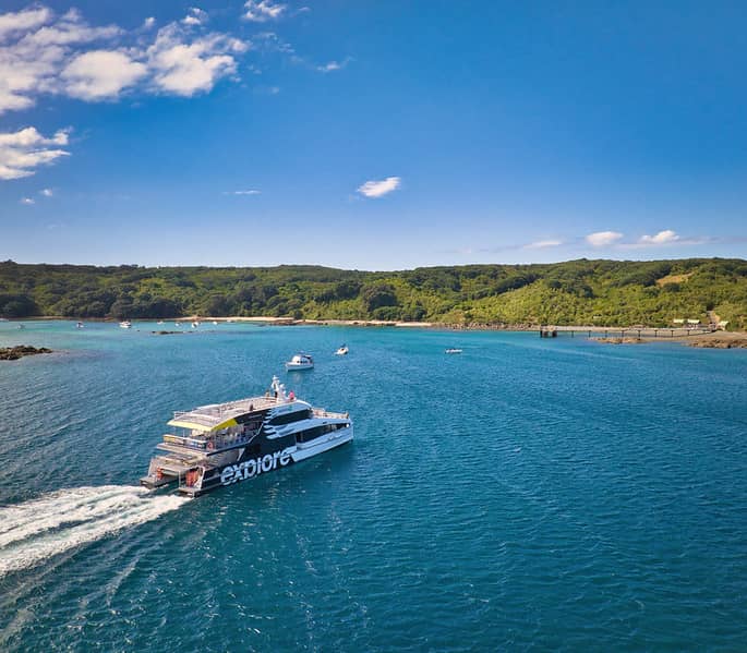 Boat with Explore Ltd logo sailing near a green coastline under a blue sky with clouds.