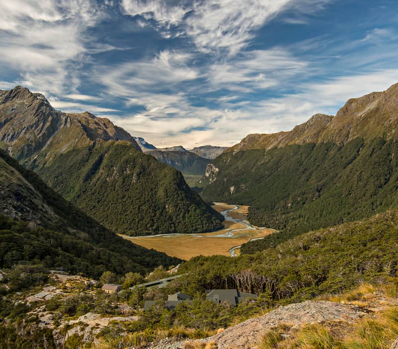 Scenic mountain valley with forest, winding river and partly cloudy sky.