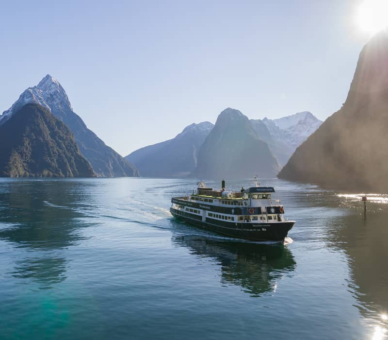 Milford Mariner cruise ship sails in misty fjord surrounded by tall mountains and cloudy skies.