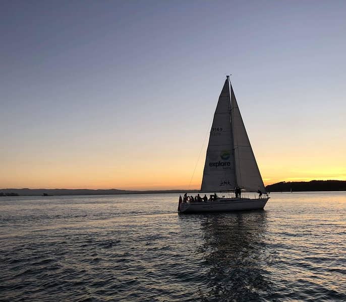 Sailboat with people sailing on calm water at sunset with a clear sky.