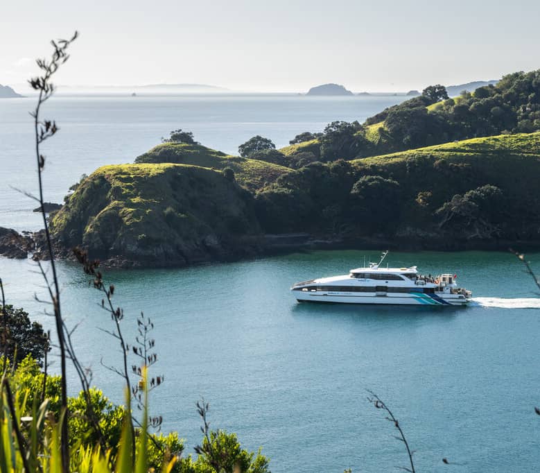 Ferry cruising in blue ocean beside green hills and trees on an island.