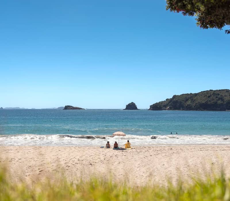 Couple relaxing on warm sand of Hahei Beach Coromandel.