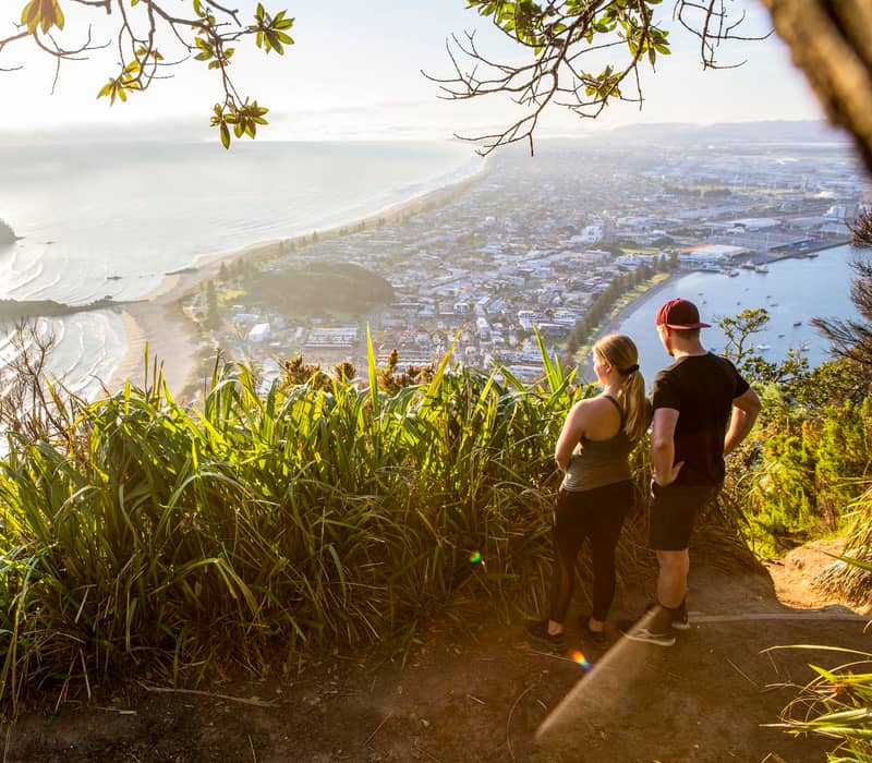 Couple looking at view of Mount Maunganui township from the Mount walking track. 