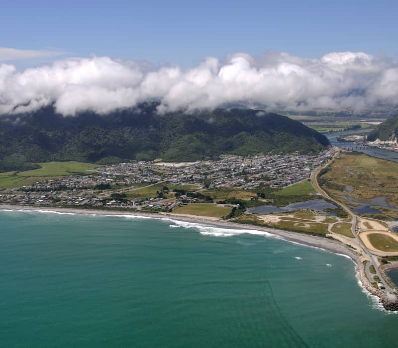 Aerial shot of Greymouth town by the coast with mountains and clouds in background