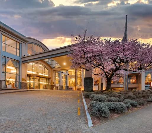 Entrance of Millennium Hotel Queenstown with glass windows and a blooming cherry blossom tree at sunset. Credit: Millennium Hotel Queenstown