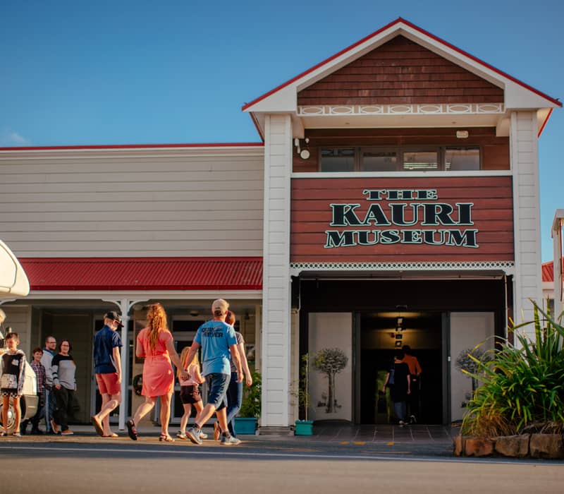 Group of people walking into The Kauri Museum building with red roof and clear blue sky Credit: Northland NZ