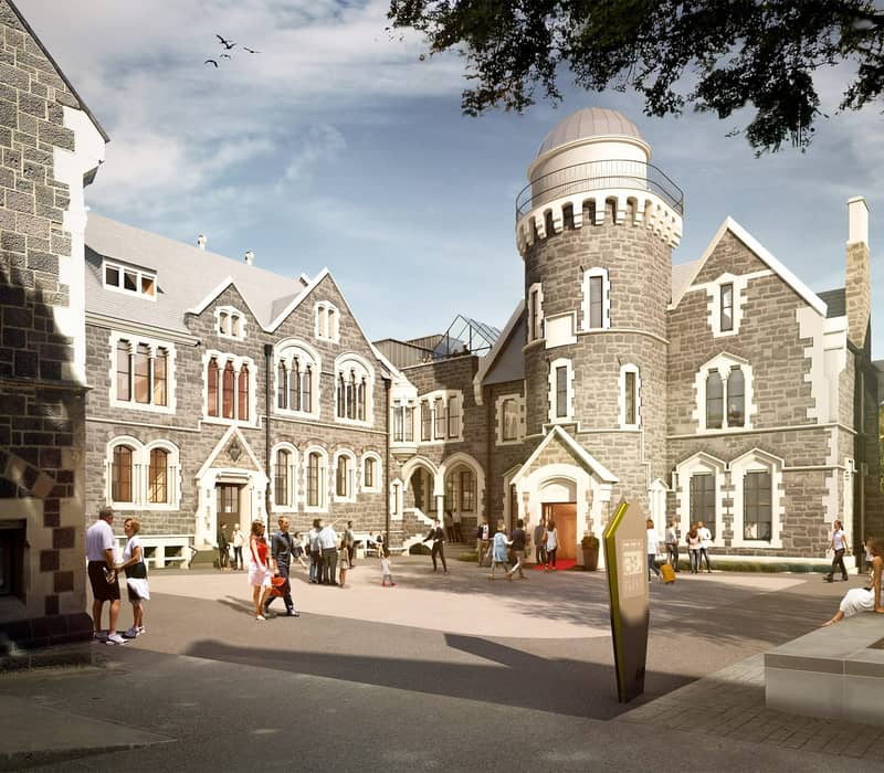 People walking and sitting outside the stone Observatory Hotel with a tower under a partly cloudy sky.