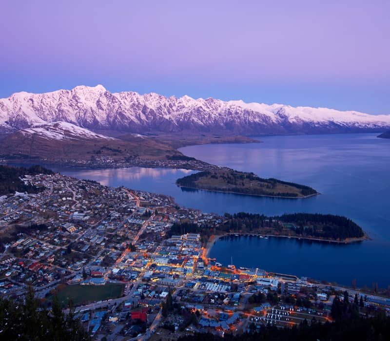 Aerial image of Queenstown at dusk with snow-covered mountains and lake in winter.