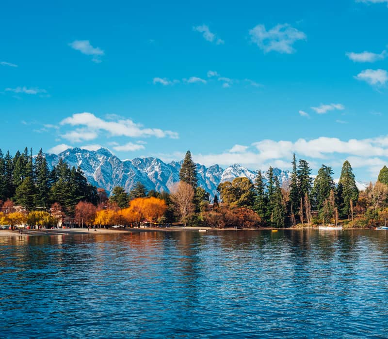 Autumn trees and snow-capped mountains reflected in lake water at Queenstown.