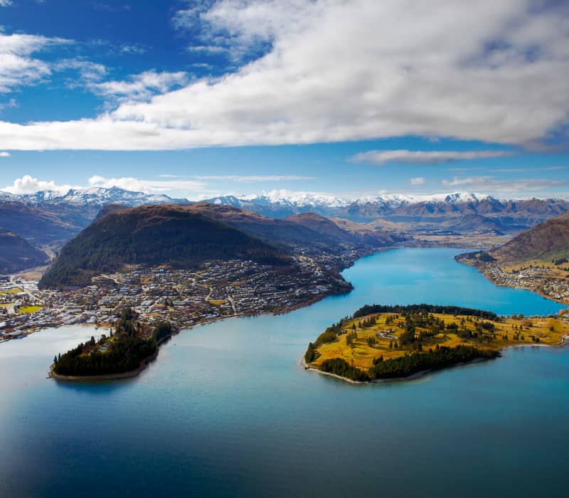 Aerial view of Queenstown and Frankton around a lake with mountains and partly cloudy sky