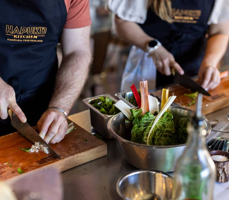 Hands chopping rainbow chard leaves on cutting boards with bowls and ingredients on counter