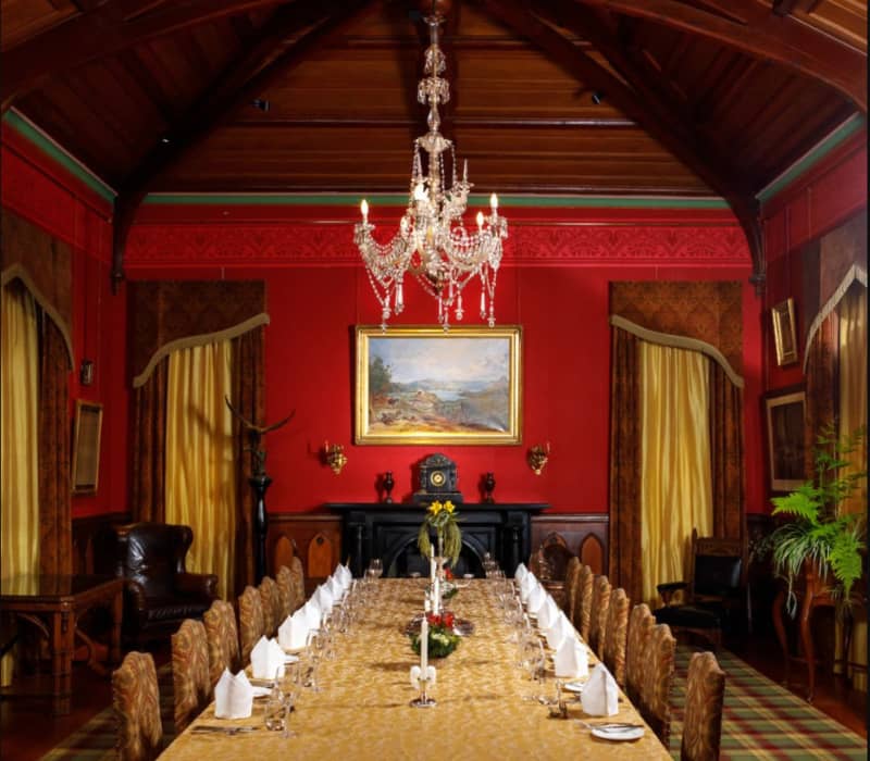 Ornate dining room with long table, chandelier, red walls, paintings, and classic furnishings.