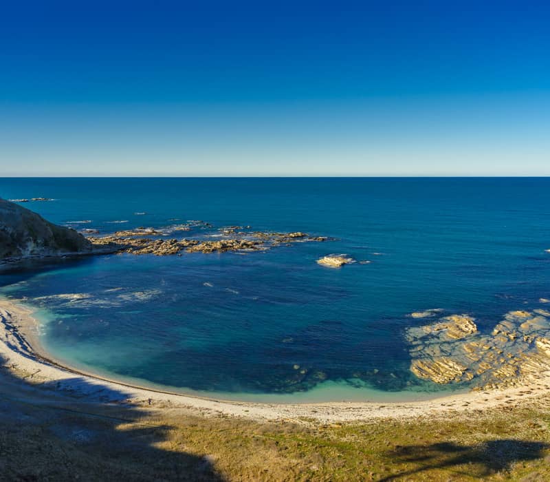 Clear blue ocean and rocky beach forming a curved bay under sunny blue sky.