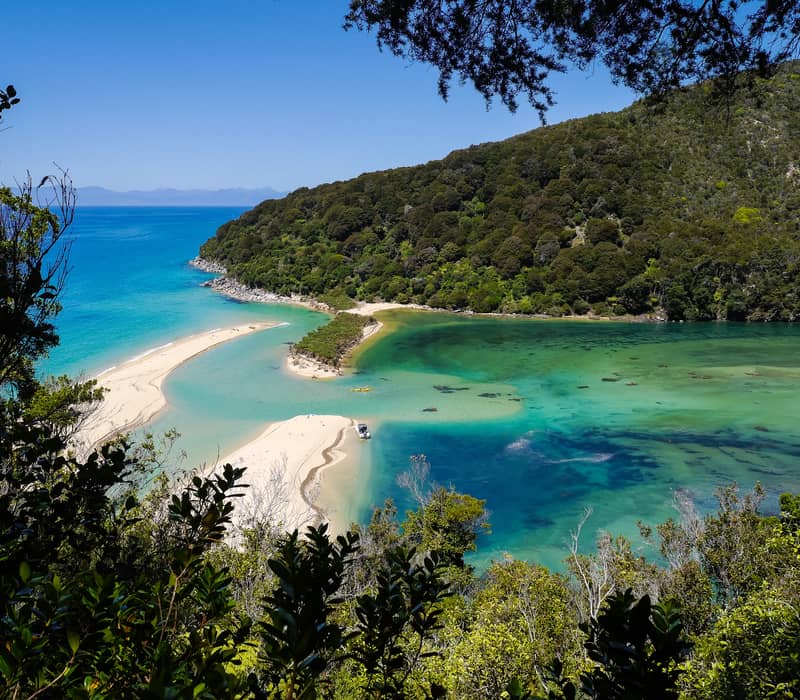 A white sandbar separates a deep blue ocean from a turquoise tidal lagoon and forest.