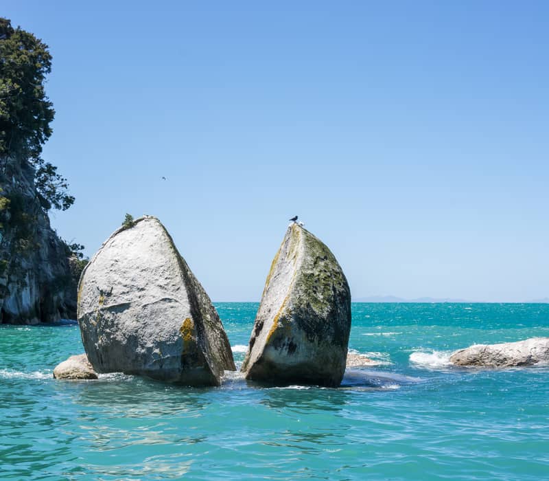 A giant circular granite rock split in two sitting in bright turquoise water.