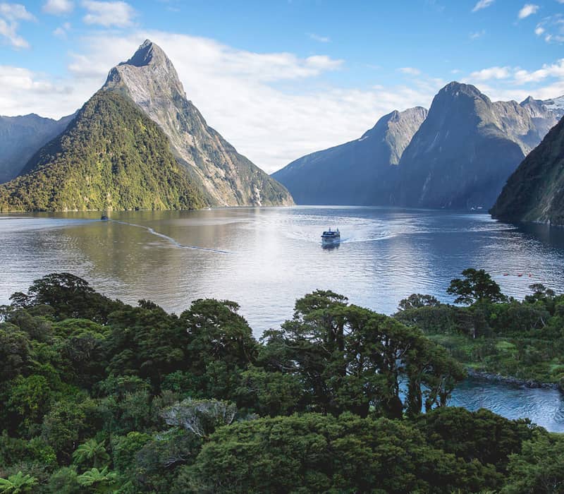 Milford Sound with a cruise boat, surrounded by mountains and lush greenery.