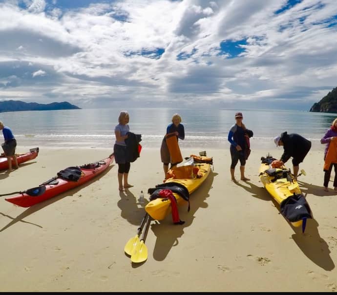 People prepping kayaks on sandy beach with calm sea and cloudy sky.