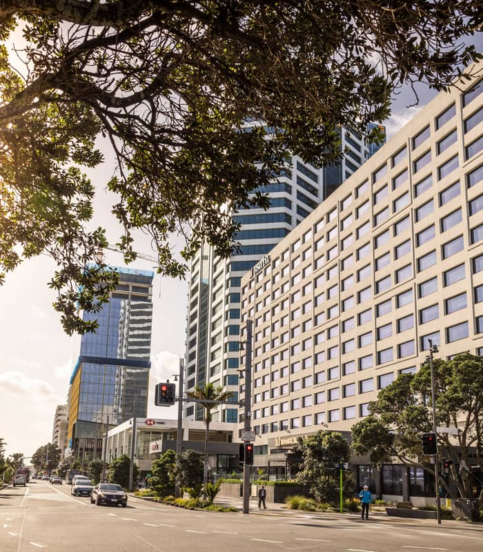 M Social Hotel Auckland building on a sunny day with street, cars, and trees in front.