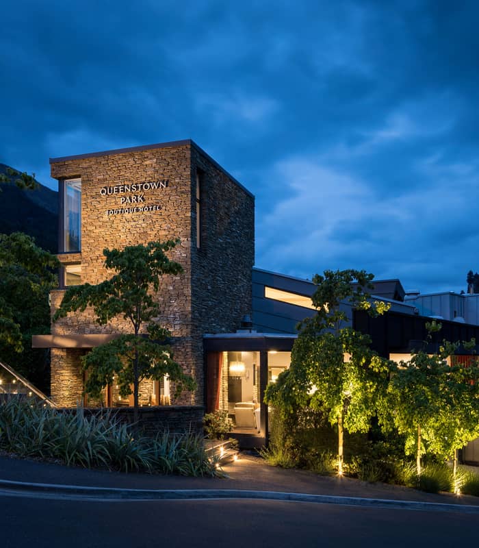 Twilight view of Queenstown Park Boutique Hotel exterior with stone facade and lit trees.