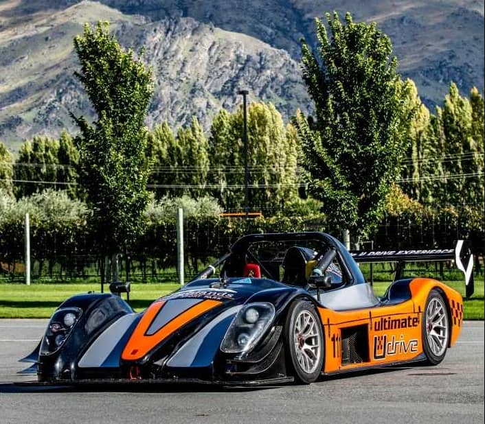 Black and orange race car parked with mountains and trees behind