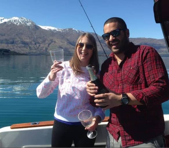 Couple celebrating on a fishing boat with champagne and glasses on a lake with mountains.