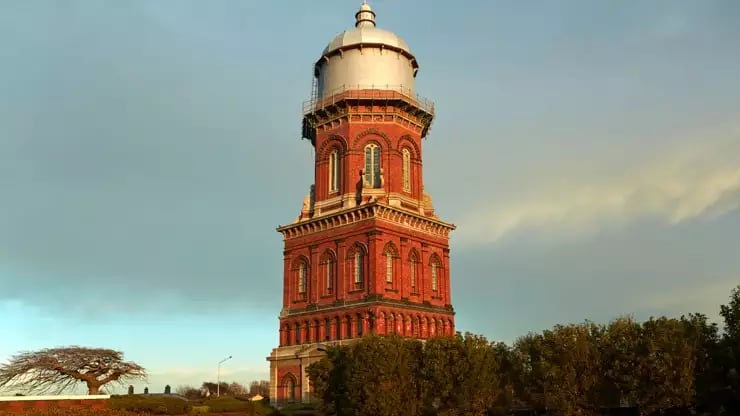 Historic red brick water tower at sunset surrounded by greenery in Invercargill. Credit: Fine Tours Group