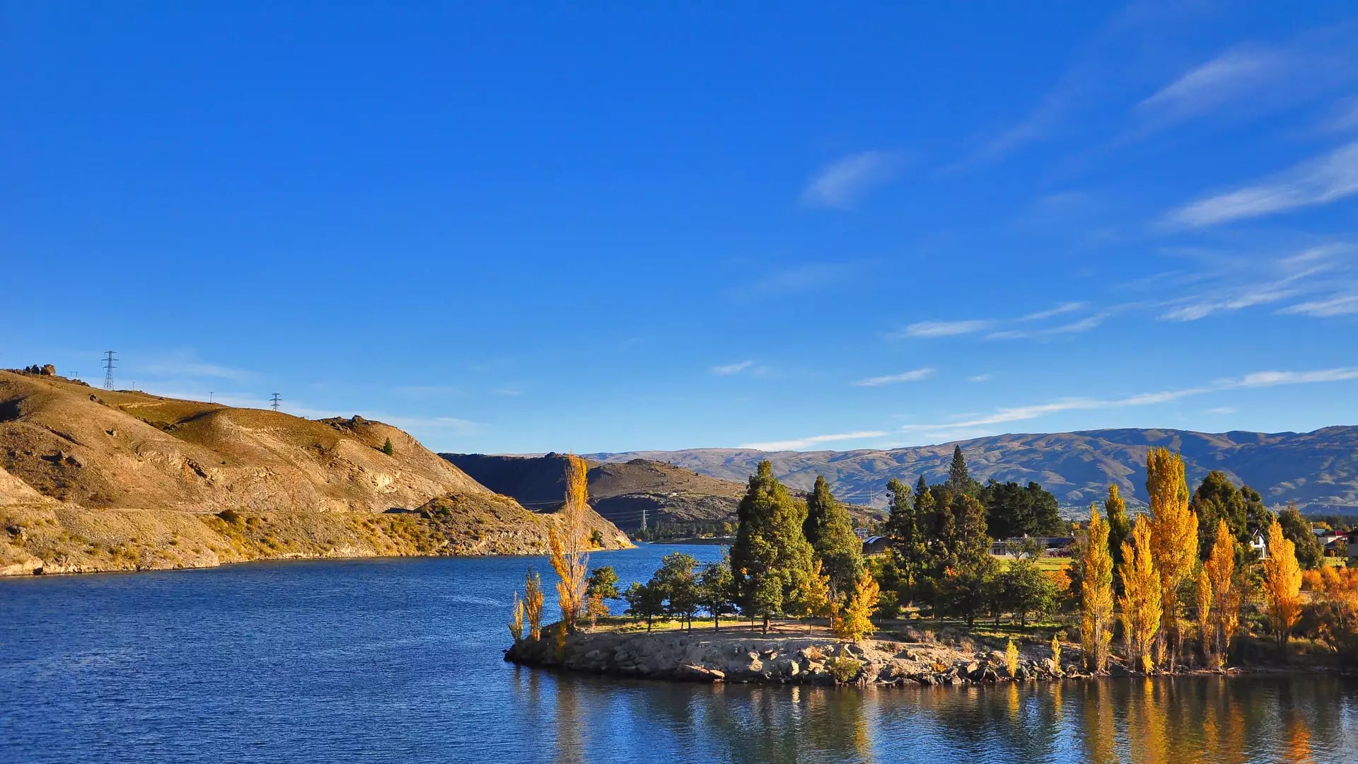 Lake with autumn trees and hills under clear blue sky reflecting on the water surface.