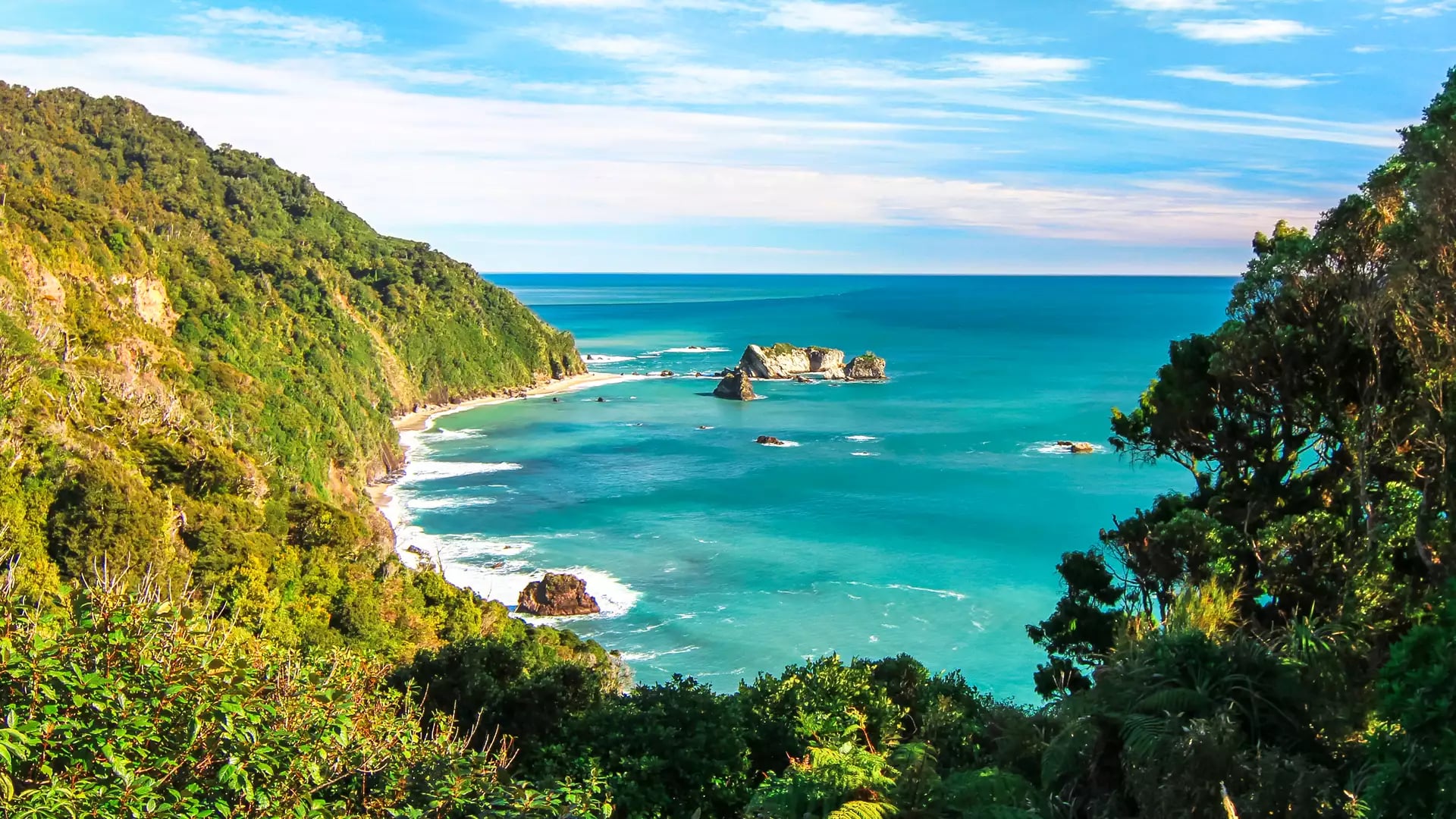 Blue sky background with a Rainforest mountain in the foreground that meets the turquoise blue sea. 