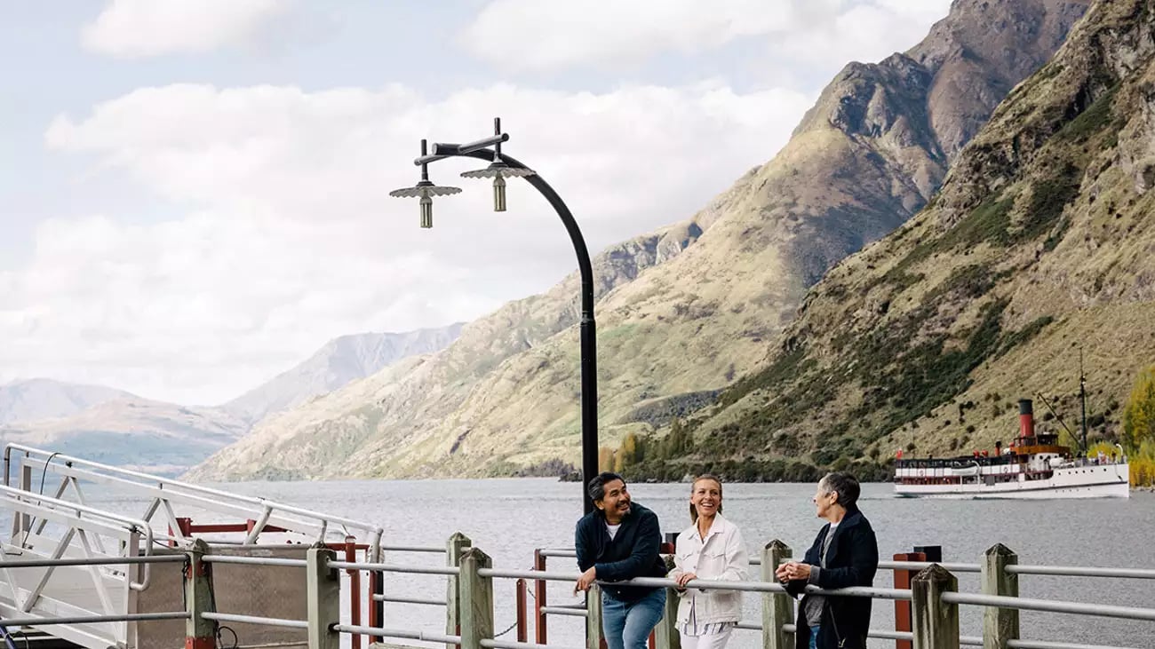 Visitors on a pier overlooking a lake with a steamship at Walter Peak High Country, Queenstown.