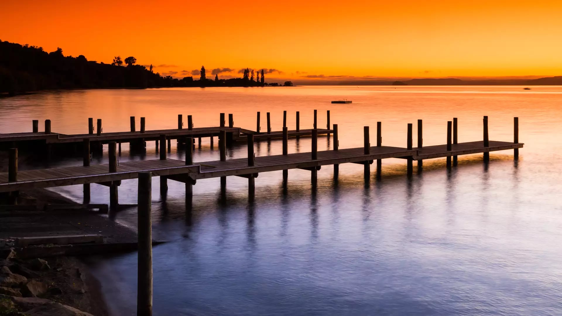 Wooden jetties on Lake Taupo at sunset with orange sky reflecting on calm water.