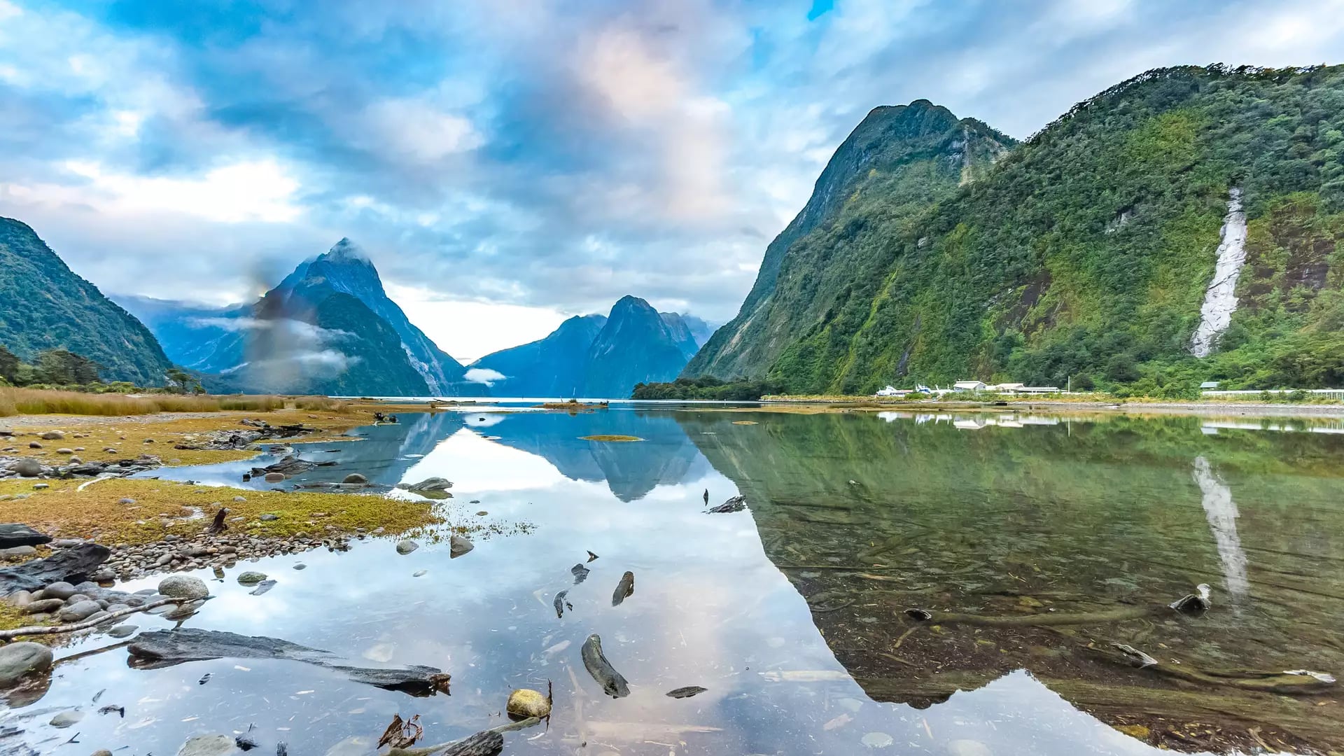 Milford Sound fjord with mountains reflected in calm water under a cloudy sky.