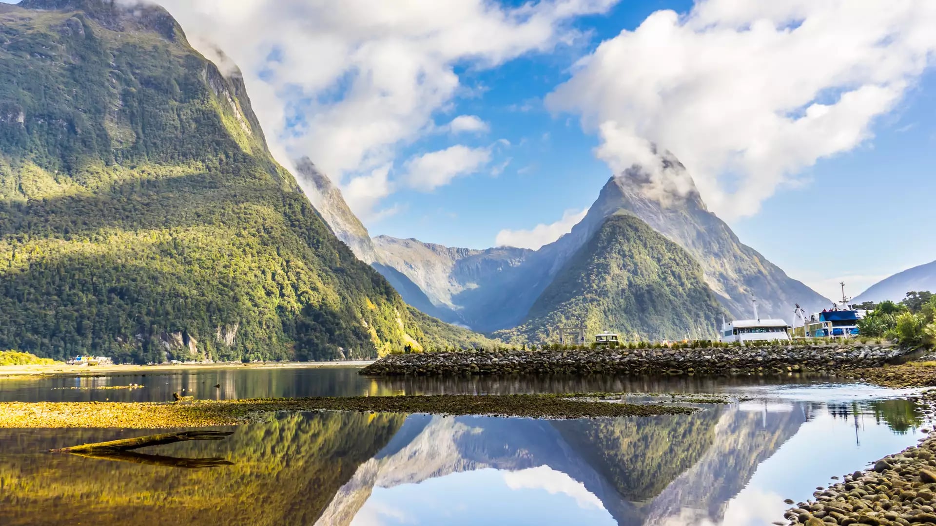 Mountains and clouds reflecting clearly in calm water at Milford Sound, New Zealand.