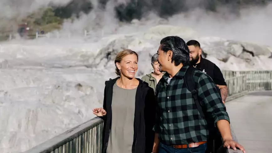 People walking by the steaming geysers in Rotorua, New Zealand.