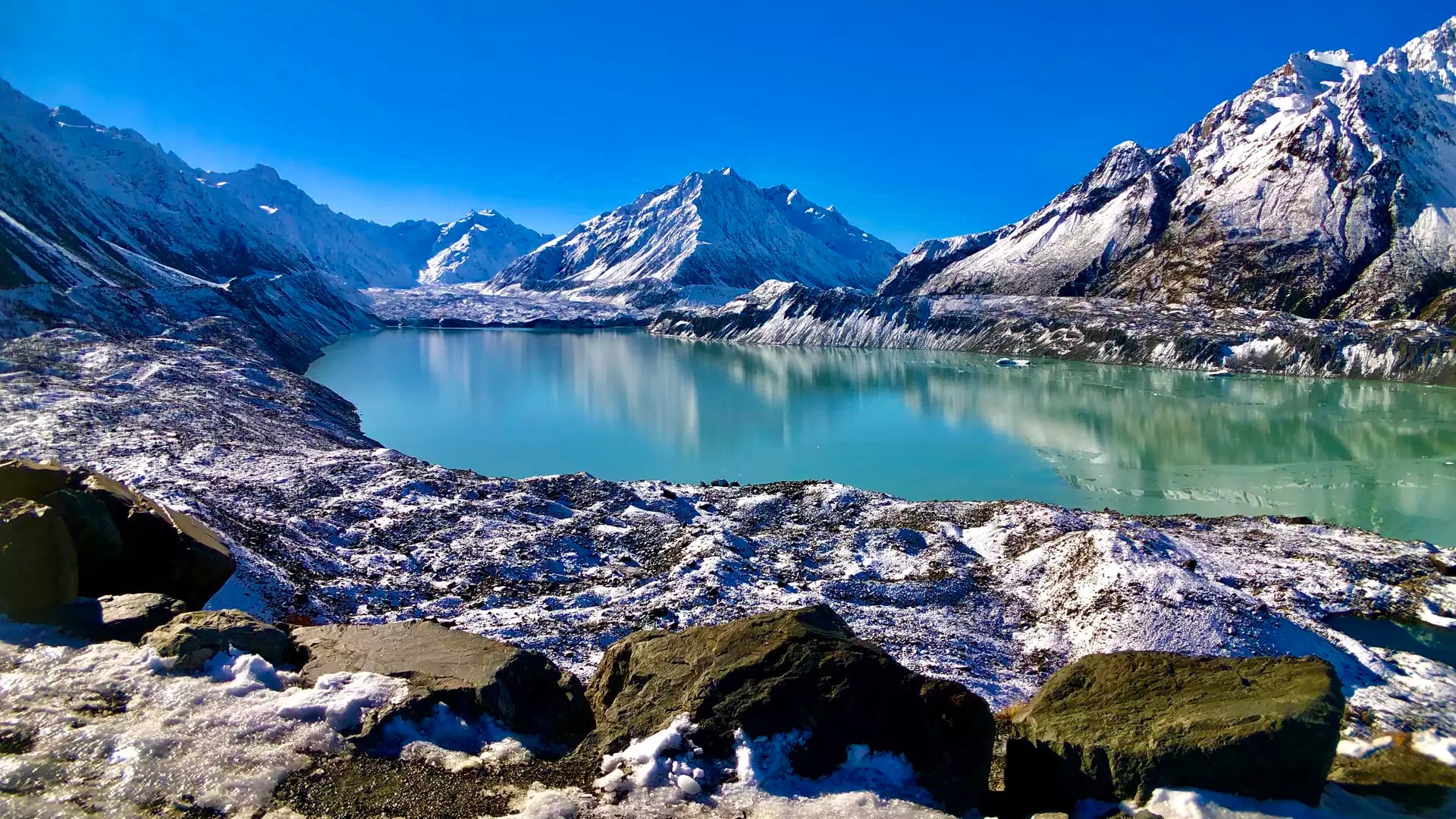 Glacial lake with snowy mountains and rocks under clear blue sky