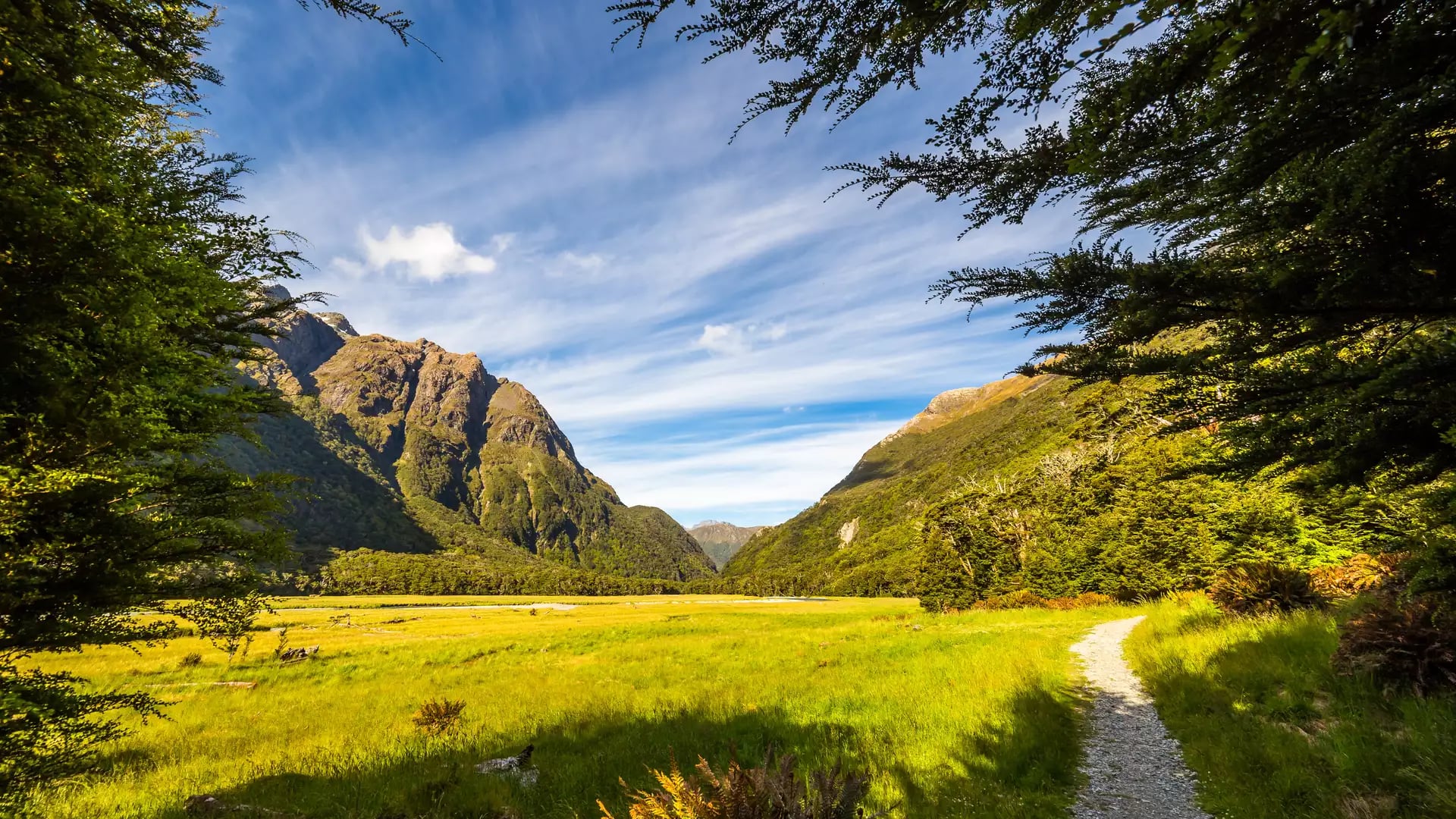 Gravel path winding through a green valley with mountains and blue sky in the background