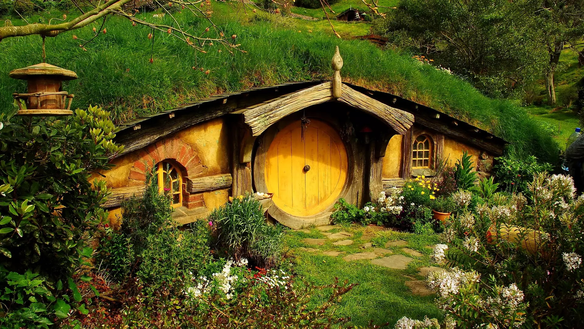 Hobbit house with round red door surrounded by flowers and greenery in Hobbiton