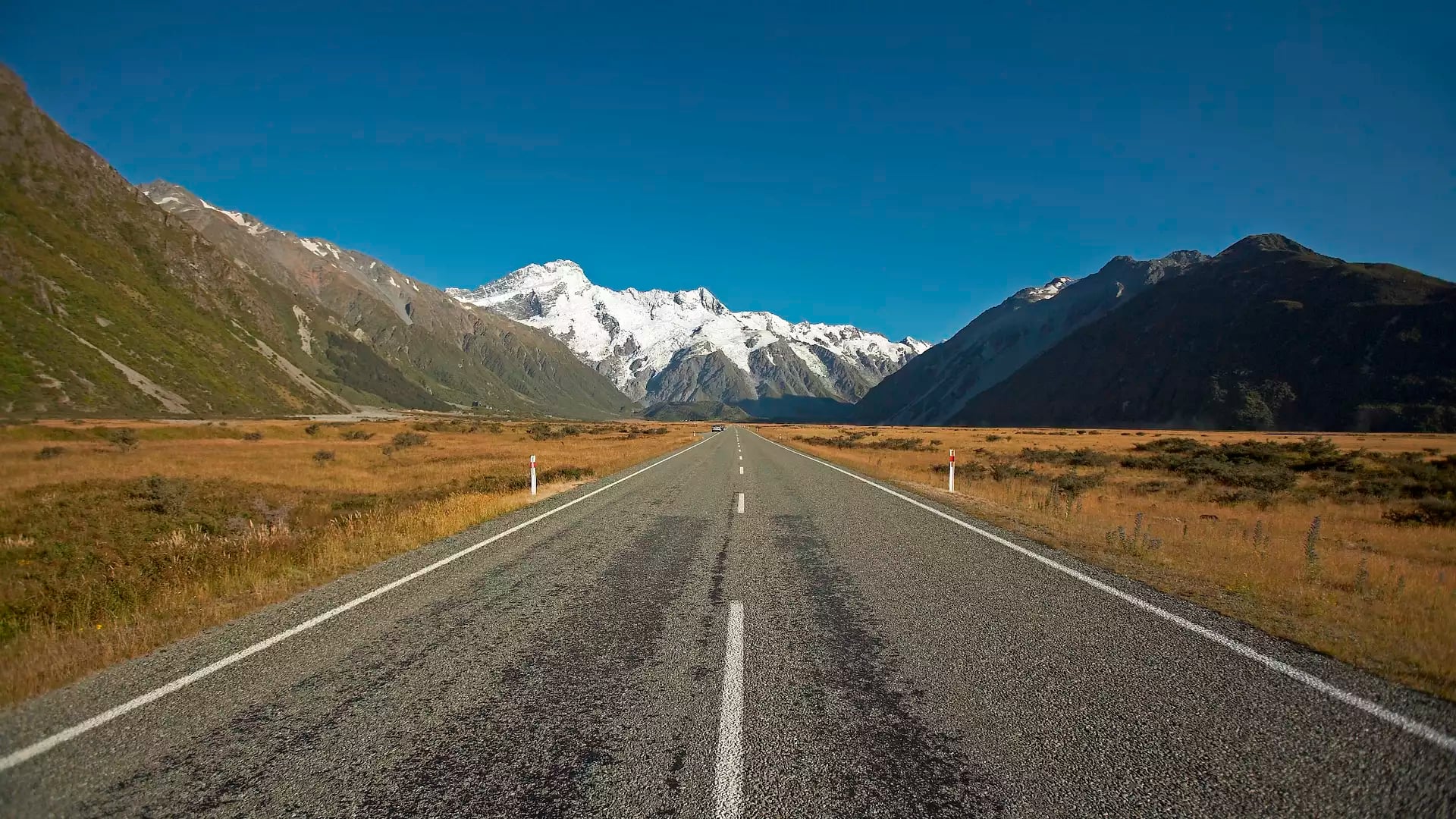 Road stretching towards snow-capped Aoraki Mount Cook with mountains and clear blue sky
