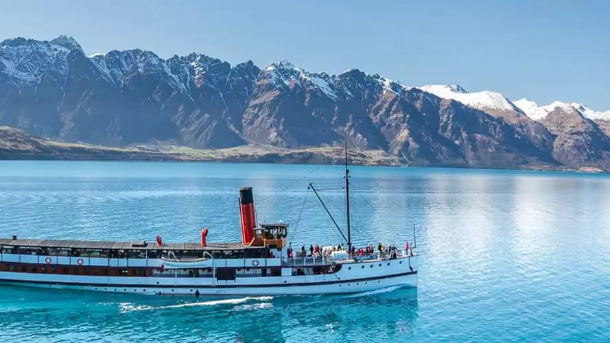 Steamship on lake with snow-capped mountains in New Zealand.