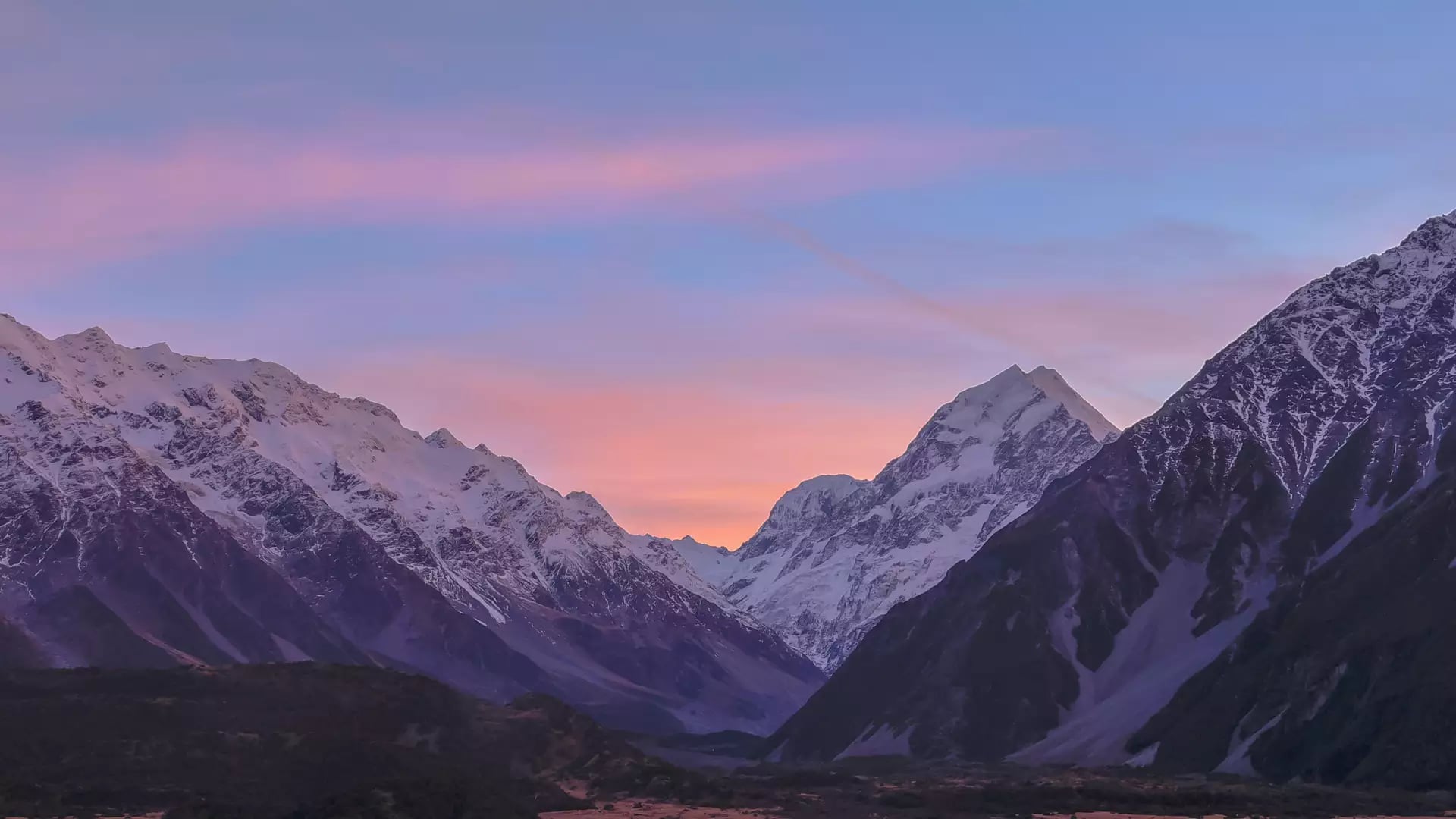 Snow-covered mountain peaks of Aoraki Mount Cook at sunset with a colorful sky.