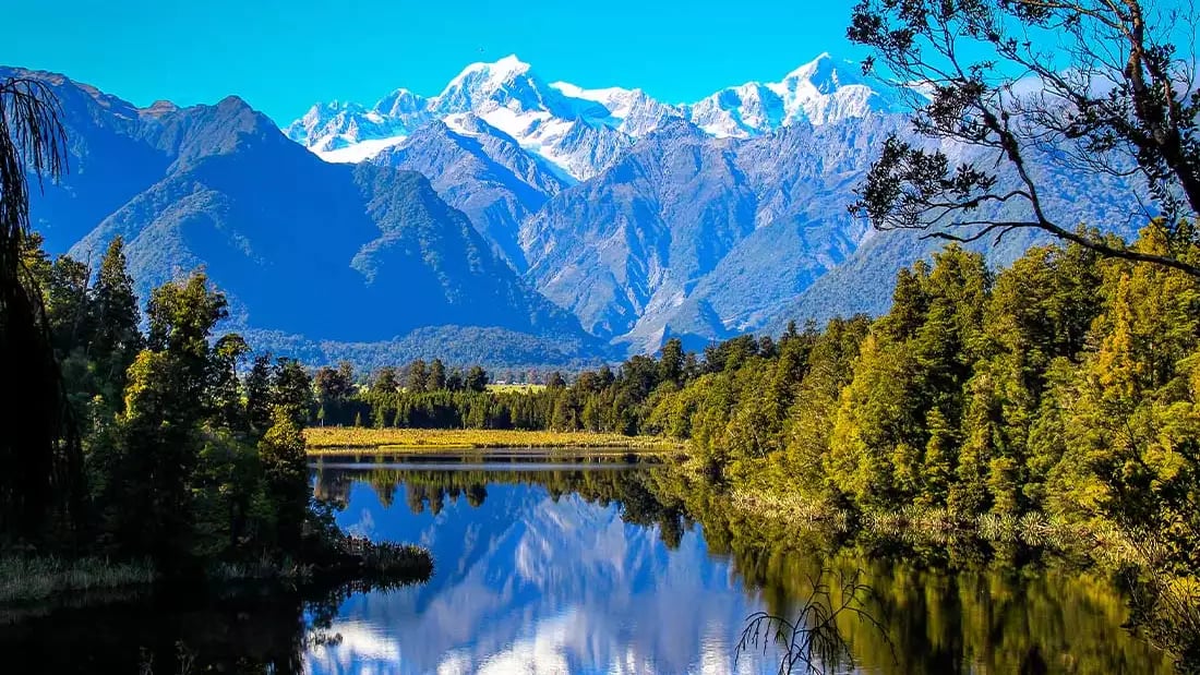 Snow-capped mountains and forest reflected in a clear lake, South Island, New Zealand.