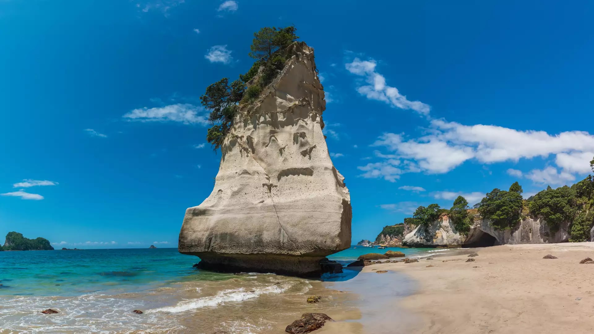 Tall rock formation on sandy beach with blue ocean and sky at Cathedral Cove, Coromandel