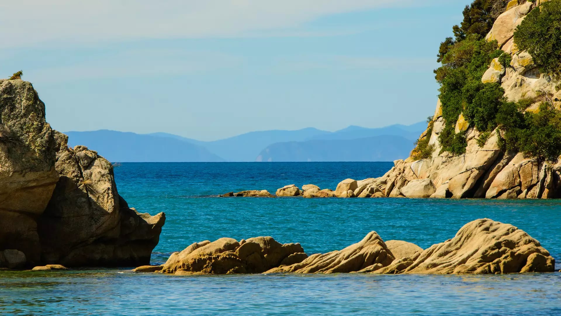 Large granite boulders and rock formations on the edge of a clear blue ocean.