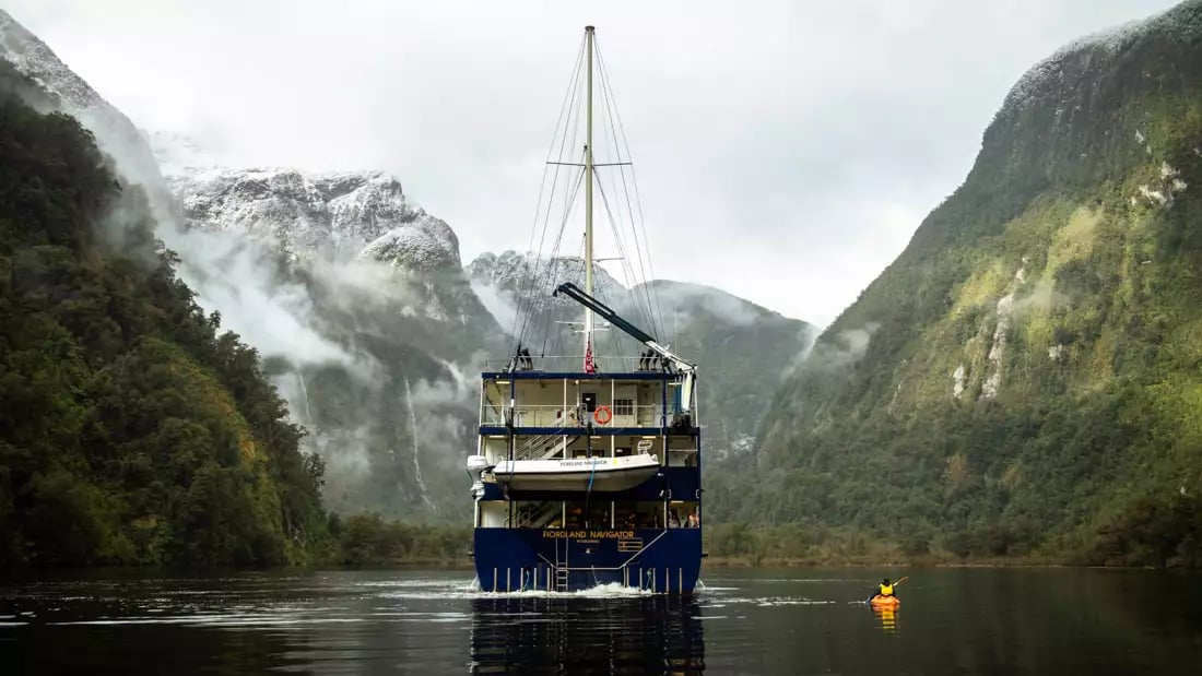 Cruise ship in New Zealand's South Island amidst misty mountains.