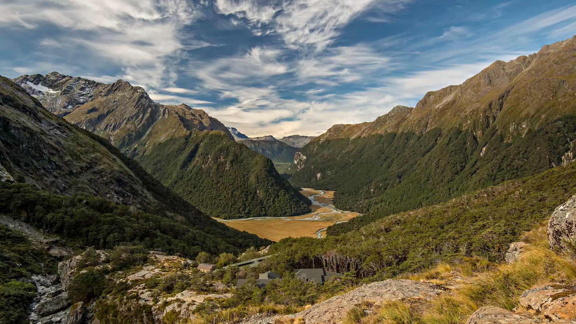 Scenic mountain valley with forest, winding river and partly cloudy sky.