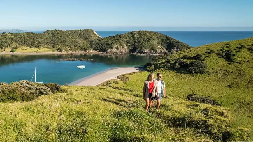 Couple hiking in Bay of Islands with scenic view of bay and boat.