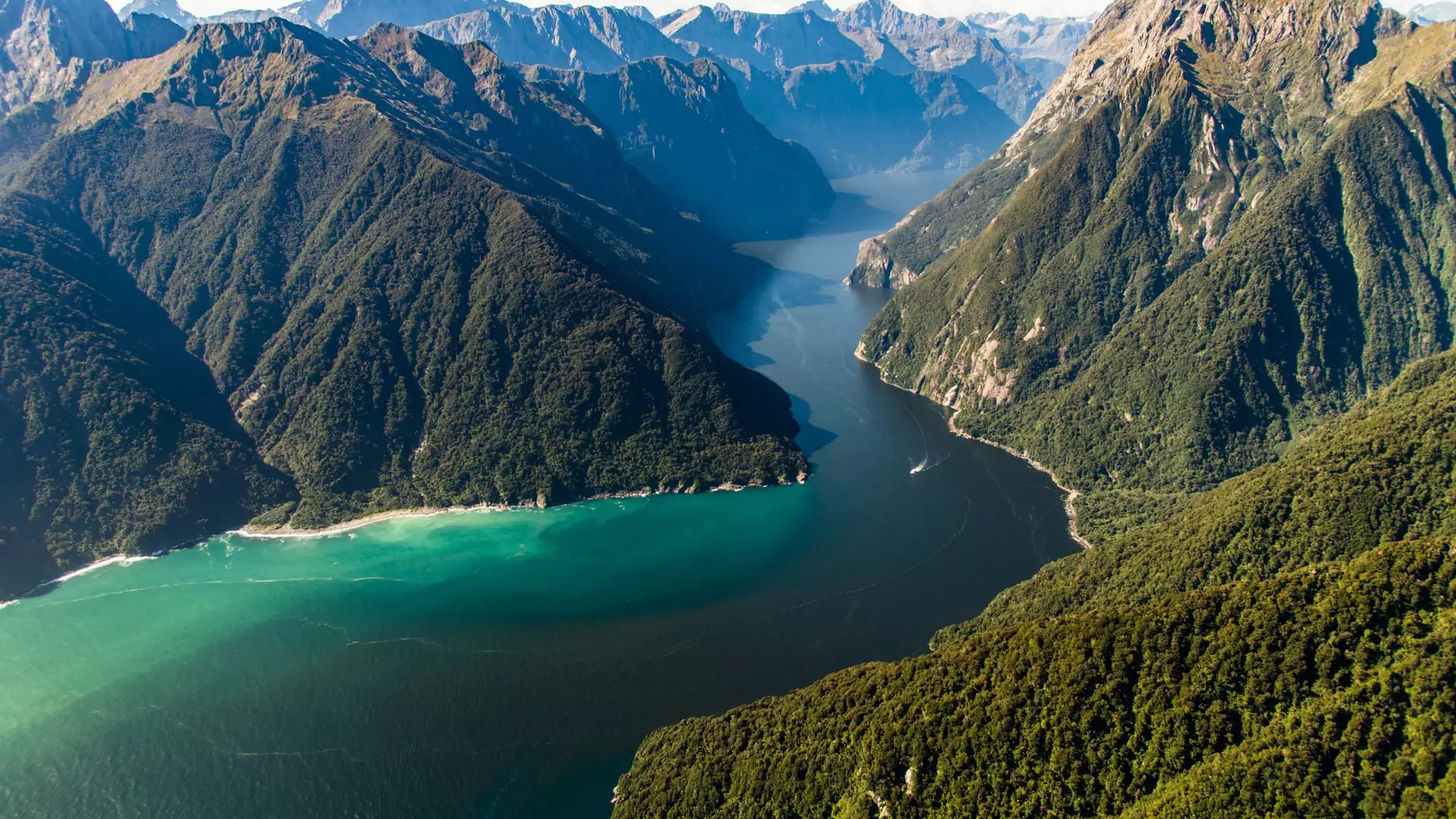 An aerial view of steep green hills with a deep blue water channel running down the middle 